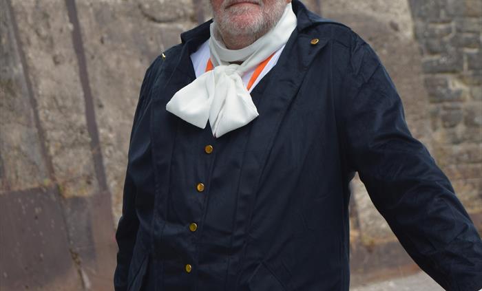 A tour guide dressed up as an 19th Century industrial factory owner standing leaning against a barrier.